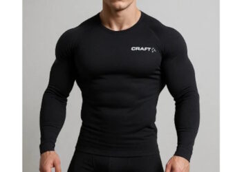 Очень накачанный блондин с короткой стрижкой позирует в чёрном термокостюме Craft, стоя на светлом фоне, с прямым уверенным взглядом и подчёркнутой мускулатурой.