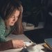 Українка ввечері за столом зі смартфоном і чашкою чаю планує місяць